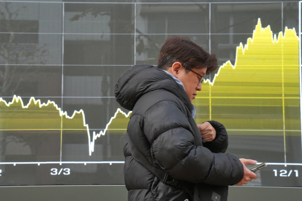 A person walks in front of a chart showing Japan's Nikkei index at a securities firm Friday, Dec. 19, 2025, in Tokyo. (AP Photo/Eugene Hoshiko)
