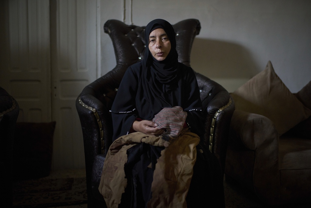 Wafa Jazar, 42, sits for a portrait, holding the clothes that her 14-year-old son, Ahmad Jazar, was wearing when he was shot by Israeli soldiers, at their home in the West Bank village of Sebastia, March 11, 2025. (AP Photo/Leo Correa)