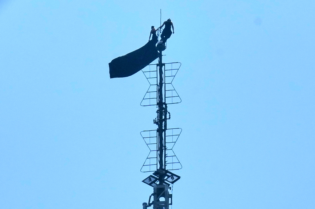 Two people stand on the tip of the antenna of the Empire State Building while holding a banner on Wednesday, July 1, 2026. (AP Photo/Richard Drew)