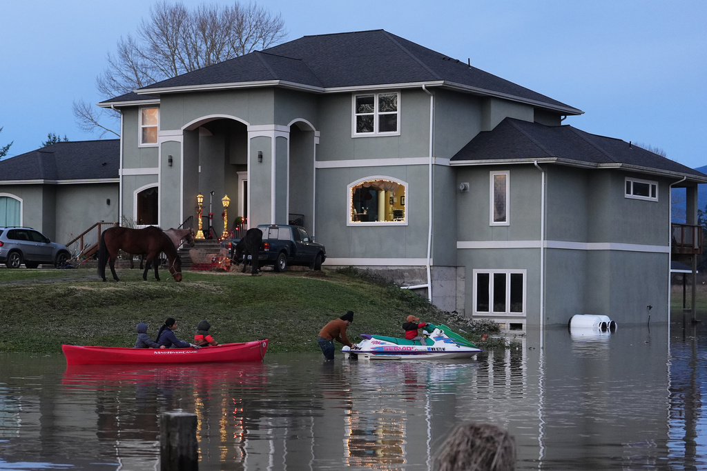 "E-man" Trujillo, center, uses a jet-ski to tow a canoe with his children Liam, 6, far left, Julissa, 15, and Benjamin, 5, third from left, as their horses take refuge on the high ground at their front door after heavy rains led to historic flooding in the region Saturday, Dec. 13, 2025, in Burlington, Wash. (AP Photo/Lindsey Wasson)