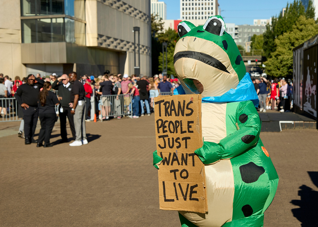 A man dressed in a frog costume holds a sign supporting trans people during a rally to support Indiana Fever guard Sophie Cunningham after her comments on transgender athletes in women's sports before a WNBA basketball game between the Portland Fire and the Indiana Fever in Portland, Ore., Friday, July 31, 2026. (AP Photo/Craig Mitchelldyer)