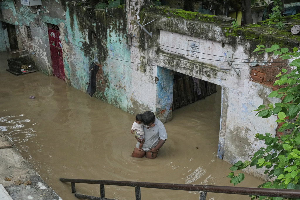 A resident carries his son and wades through floodwater after the river Yamuna, swollen by incessant rain in the higher regions, overran its banks, in New Delhi, India, Tuesday, Sept. 2, 2025. (AP Photo/Manish Swarup)