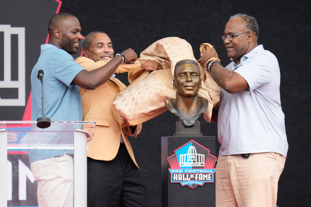 Former NFL player Roger Craig, center, unveils his bust with son, Roderick Craig, left, and Jamie Williams during the Pro Football Hall of Fame induction ceremony at the Pro Football Hall of Fame, in Canton, Ohio, Saturday, Aug. 8, 2026. (AP Photo/Sue Ogrocki)