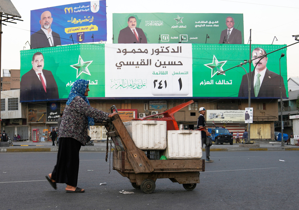 A vendor walks past an Iraqi parliamentary elections banner in Baghdad, Oct. 16, 2025. (AP Photo/ Hadi Mizban)