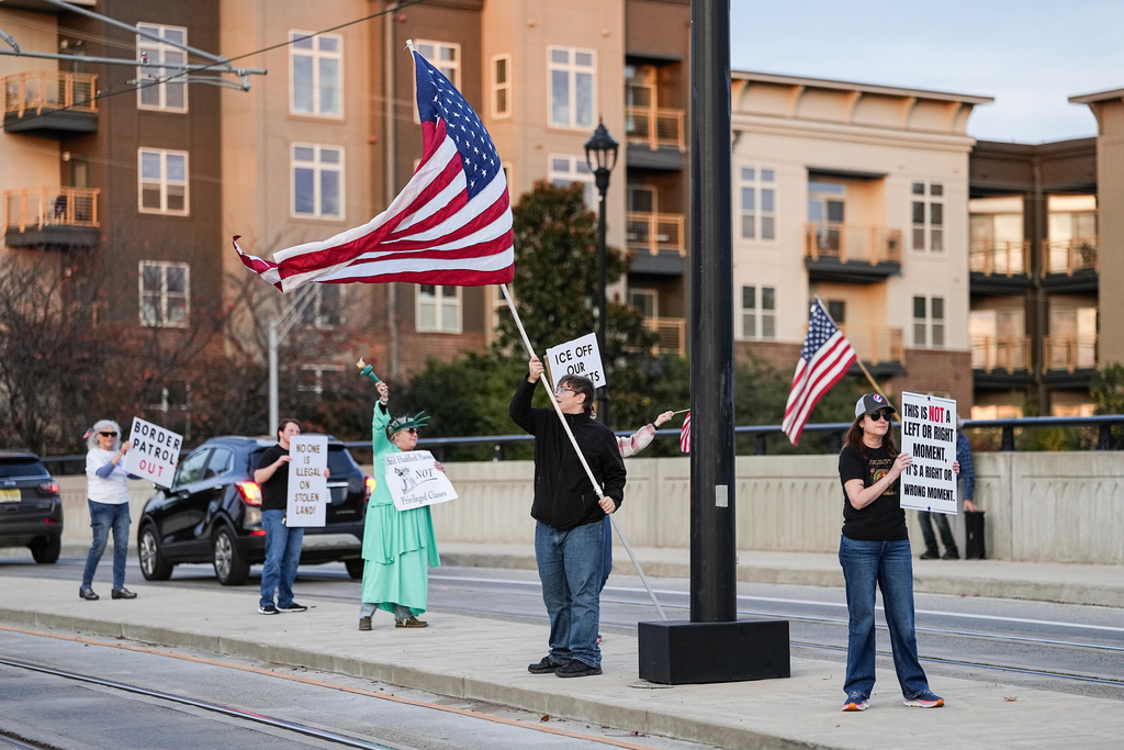 Protesters hold signs and flags amid the arrival of federal law enforcement, Tuesday, Nov. 18, 2025, in Charlotte, N.C. (AP Photo/Matt Kelley)