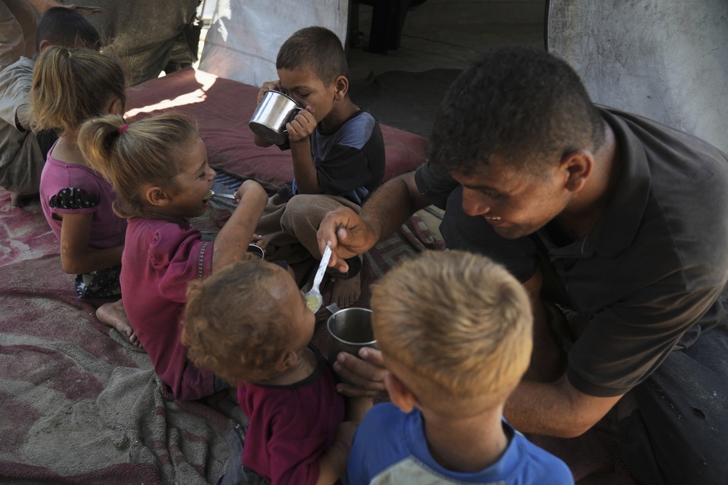 Fadi Sobh gives lentil soup to his children as they sit in their tent at a camp for displaced Palestinians in Gaza City, July 24, 2025. (AP Photo/Jehad Alshrafi)