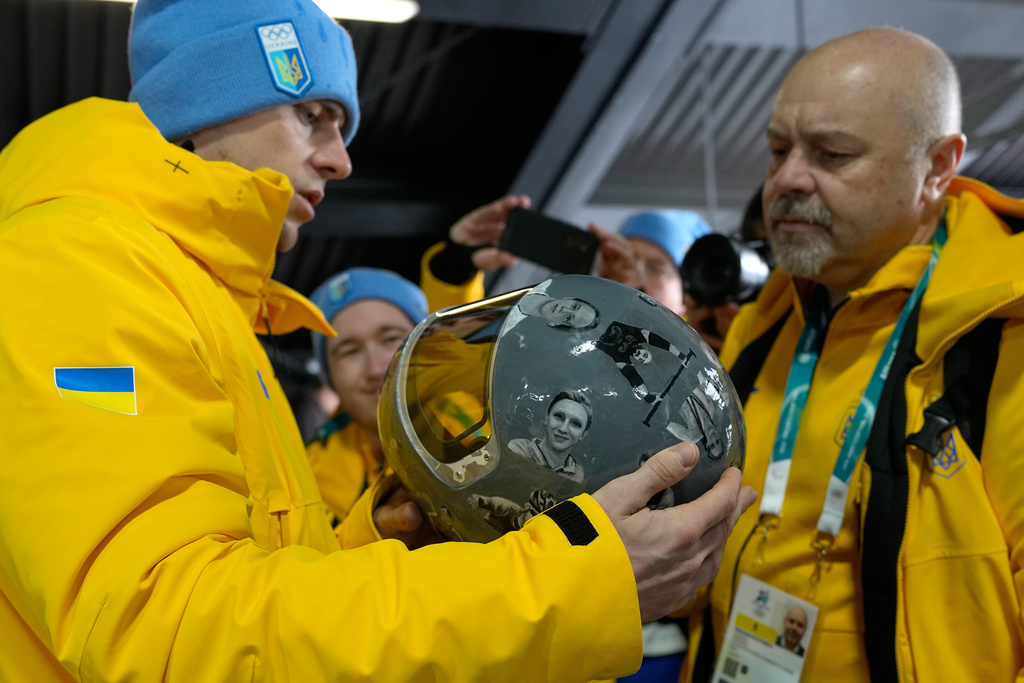 Ukrainian skeleton athlete Vladyslav Heraskevych left, holds his crash helmet at the mixed zone of the sliding center at the 2026 Winter Olympics, in Cortina d'Ampezzo, Italy, Thursday, Feb. 12, 2026. (AP Photo/Alessandra Tarantino)