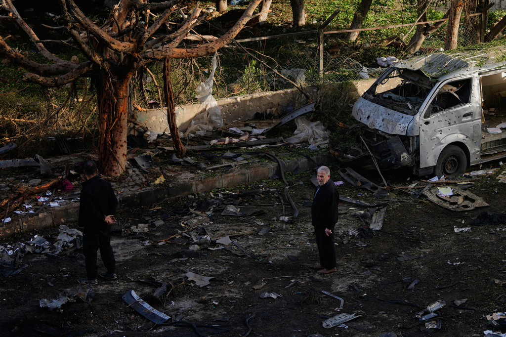 People stand near a damaged van beside scattered debris following an Israeli strike in Beirut, Lebanon, Wednesday, April 1, 2026. (AP Photo/Hassan Ammar)