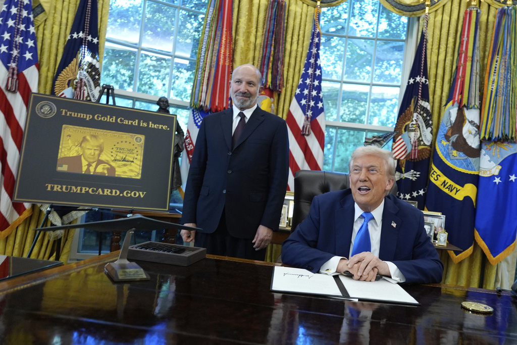 President Donald Trump speaks as Commerce Secretary Howard Lutnick listens alongside a poster of the Trump Gold Card in the Oval Office of the White House, Friday, Sept. 19, 2025, in Washington. (AP Photo/Alex Brandon)