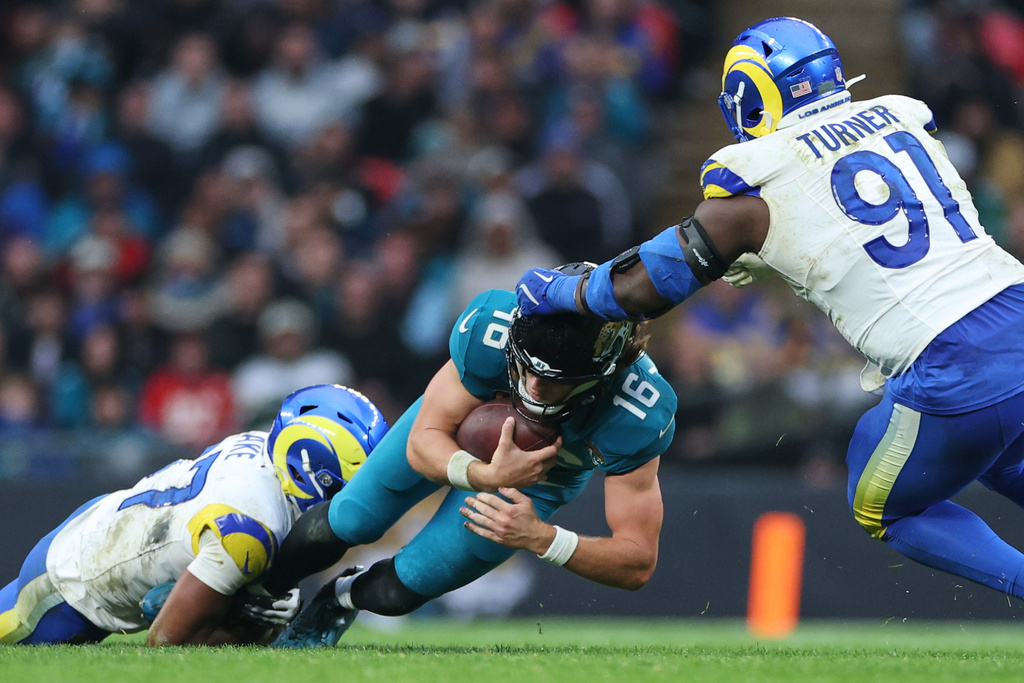 Los Angeles Rams safety Quentin Lake (37), left, and defensive end Kobie Turner (91) tackle Jacksonville Jaguars quarterback Trevor Lawrence (16) during the second half of an NFL football game between the Los Angeles Rams and the Jacksonville Jaguars in London, Sunday, Oct. 19, 2025. (AP Photo/Ian Walton)
