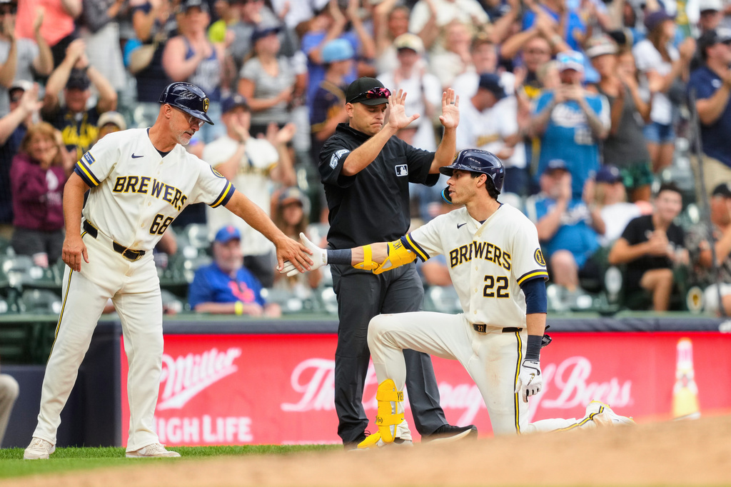 Milwaukee Brewers designated hitter Christian Yelich (22) high-fives third base coach Matt Erickson (68) after hitting an RBI triple as umpire Jansen Visconti (52) looks on during the sixth inning of a baseball game against the New York Mets, Wednesday, July 22, 2026, in Milwaukee. (AP Photo/Kayla Wolf)