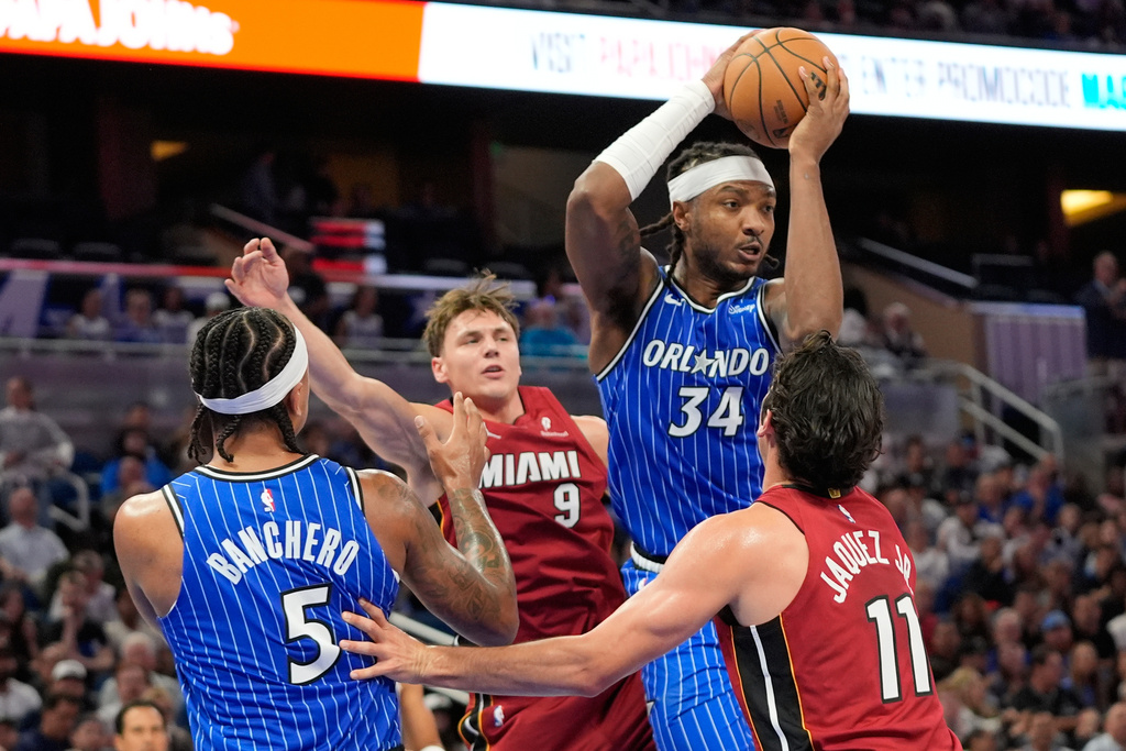 Orlando Magic center Wendell Carter Jr. (34) looks to pass the ball as he is caught between Miami Heat guard Pelle Larsson (9) and guard Jaime Jaquez Jr. (11) during the first half of an NBA basketball game, Friday, Dec. 5, 2025, in Orlando, Fla. (AP Photo/John Raoux)