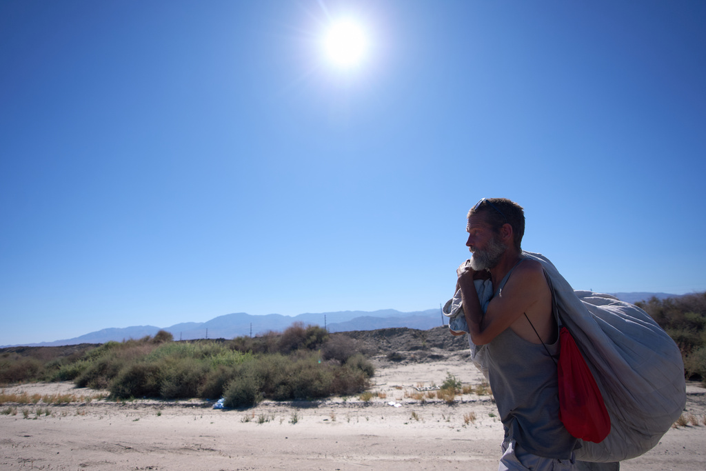 Mike Lillelund carries his belongings as he walks along a road as a record-breaking winter heat wave continues across the Southwest, Thursday, March 19, 2026, in Thermal, Calif. (AP Photo/Gregory Bull)