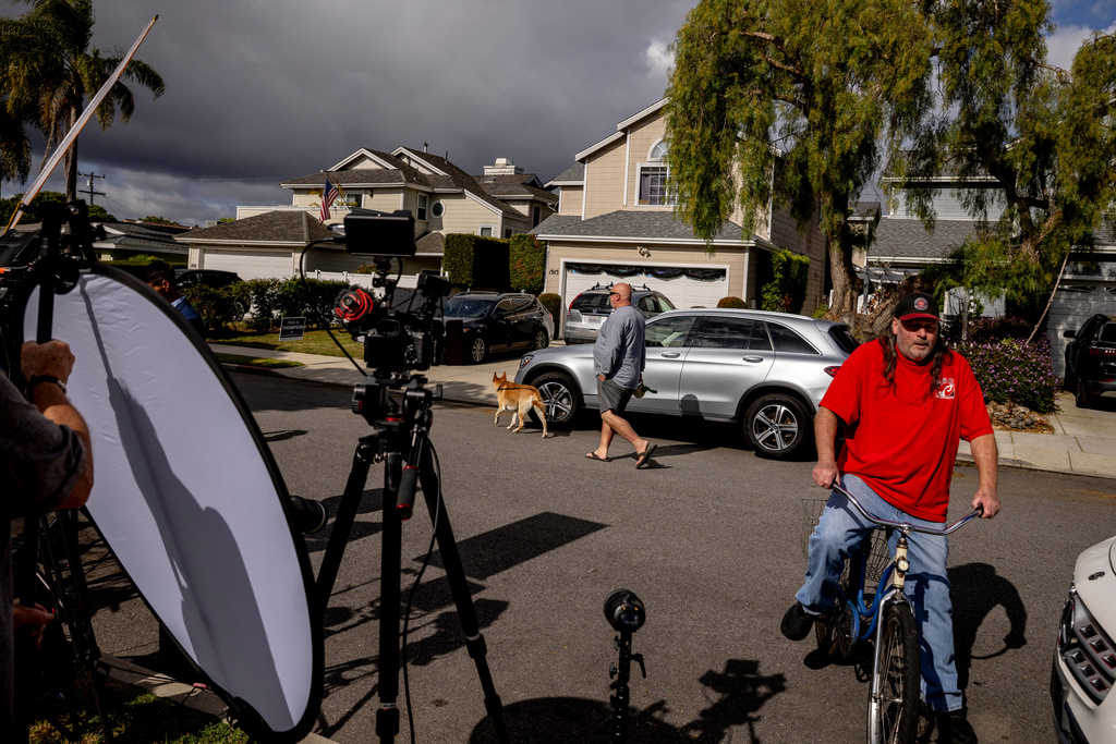 Pedestrians walk past the home, middle back, connected to Cole Tomas Allen, who was identified as the suspect at the White House Correspondents Dinner shooting, as members of the media stage, in Torrance, Calif., Sunday, April 26, 2026. (Stephen Lam/San Francisco Chronicle via AP)