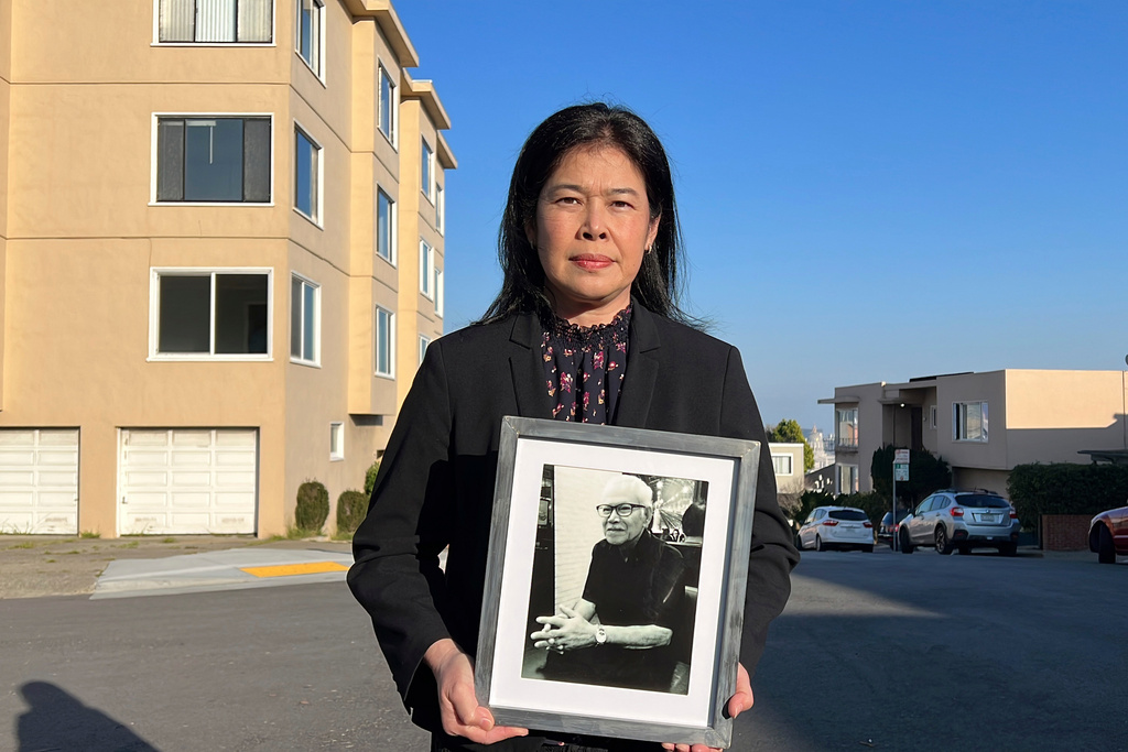FILE - Monthanus Ratanapakdee holds a photo of her father, 84-year-old Vicha Ratanapakdee, and stands in front of the San Francisco apartment building where he was attacked last year and later died of his injuries, on Jan. 26, 2022. (AP Photo/Terry Chea, File)