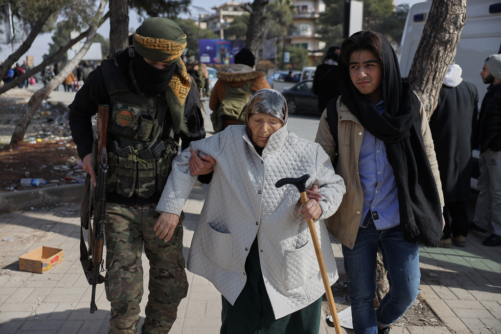 A Syrian government soldier helps an old woman who is fleeing from Sheikh Maqsoud and Achrafieh neighborhoods after clashes broke out on Tuesday between Syrian government forces and Kurdish fighters in a contested area of the northern city of Aleppo, Syria, Wednesday, Jan. 7, 2026. (AP Photo/Omar Albam)