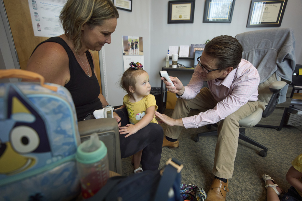 Dr. Charles Fraley, right, checks the temperature of Brooklyn Marris, center, as she arrives for a blood pressure check with her mother, Emily Marris, left, at his office in Winchester, Calif., on Thursday, Sept. 18, 2025. (AP Photo/Gregory Bull)