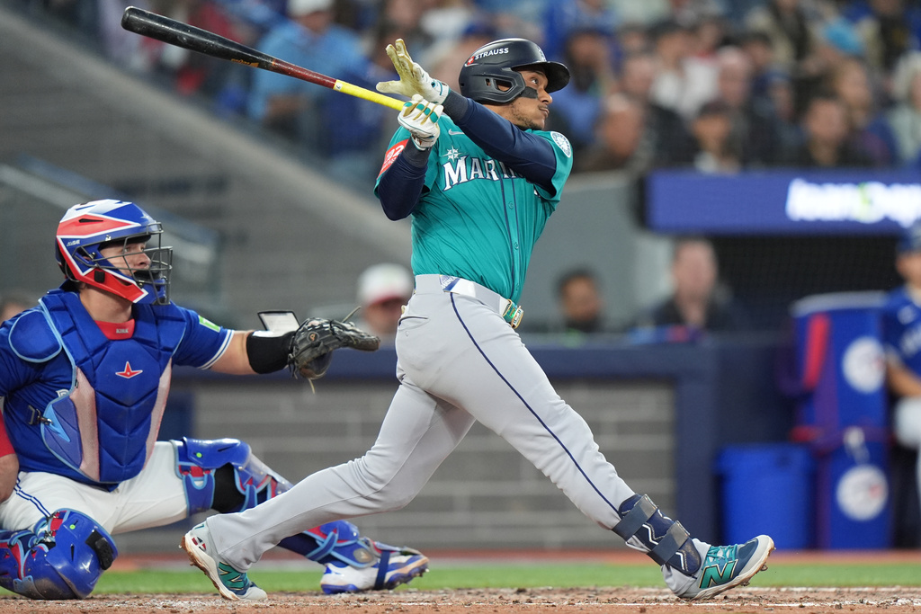 Seattle Mariners' Jorge Polanco, right, hits a three-run home run in front of Toronto Blue Jays catcher Alejandro Kirk, left, during the fifth inning of Game 2 of baseball's American League Division Series in Toronto, Monday, Oct. 13, 2025. (Frank Gunn/The Canadian Press via AP)