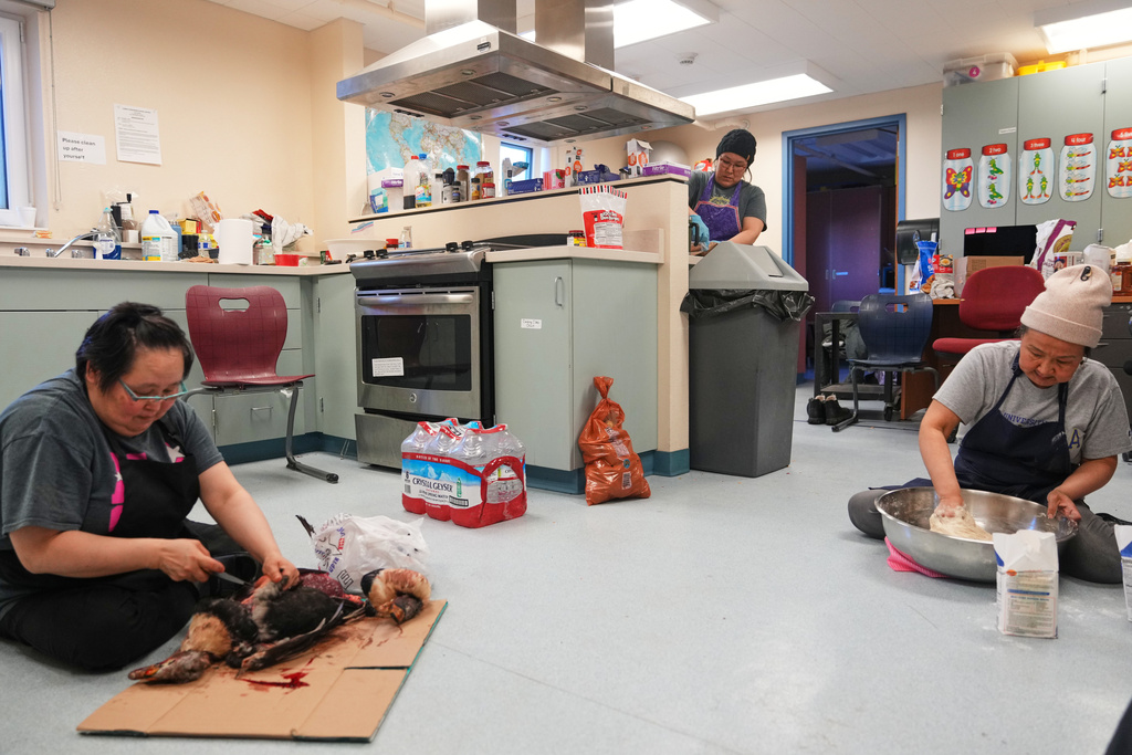 Minnie Brown, left, Patricia Twitchell, center, and Nettie Igkurak work in the school kitchen to help prepare traditional food, like King eider and fry bread, for search and rescue workers and some villagers who chose not to evacuate Kwigillingok, Alaska, Monday, Oct. 27, 2025, after Typhoon Halong hit earlier in the month. (AP Photo/Lindsey Wasson)