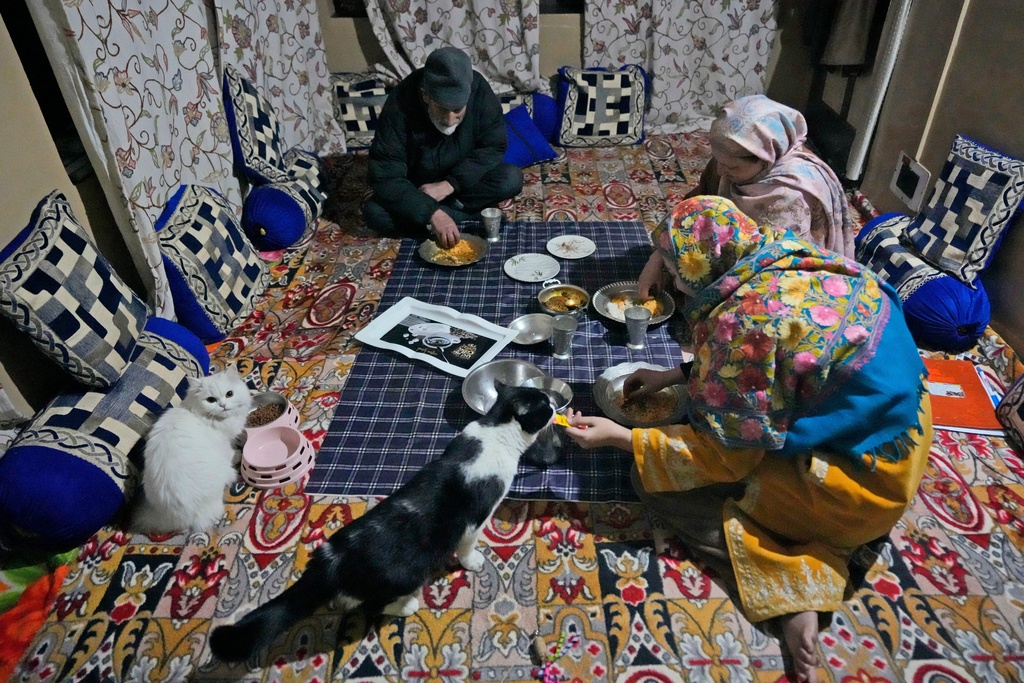 FILE - A Kashmiri family eats dinner with their pet cats sitting beside them inside in Srinagar, Indian controlled Kashmir, Feb. 12, 2025 (AP Photo/Mukhtar Khan, File)