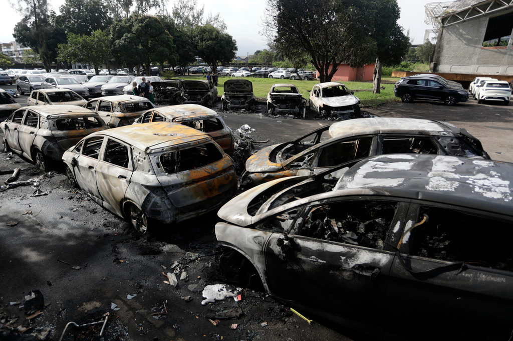 Burned vehicles fill a car dealership parking lot where, according to police, two helicopters collided in midair and crashed in Rio de Janeiro, Brazil, Sunday, June 14, 2026. (AP Photo/Bruna Prado)