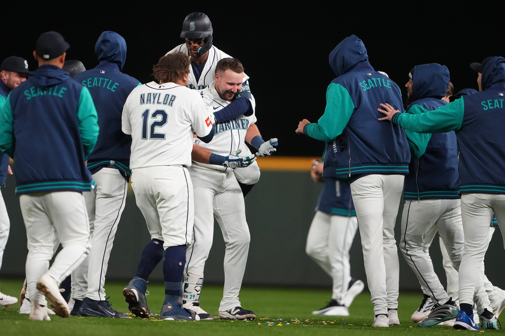 Seattle Mariners' Julio Rodríguez, top back, jumps on Cal Raleigh to celebrate Raleigh's game-winning single over the New York Yankees in a baseball game, Monday, March 30, 2026, in Seattle. (AP Photo/Lindsey Wasson)
