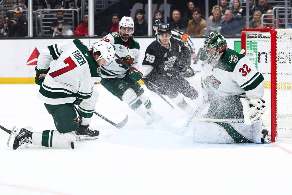 Minnesota Wild goaltender Filip Gustavsson (32) watches after making a save as Minnesota Wild defenseman Brock Faber (7) looks on at the puck as right wing Mats Zuccarello, second from left, and Los Angeles Kings left wing Jeff Malott (39) watch during the second period of an NHL hockey game, Monday, Jan. 5, 2026, in Los Angeles. (AP Photo/Jessie Alcheh)