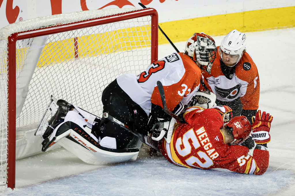 Philadelphia Flyers' Cam York, right, and Calgary Flames' MacKenzie Weegar, centre, crash into goalie Samuel Ersson during third period NHL hockey action in Calgary on Wednesday, Dec. 31, 2025. (Jeff McIntosh/The Canadian Press via AP)