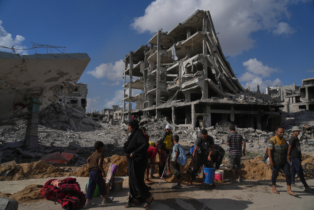 Palestinians collect water from a broken pipe surround destroyed buildings in Gaza City, Sunday, Oct. 12, 2025, after Israel and Hamas agreed to a pause in their war and the release of the remaining hostages. (AP Photo/Jehad Alshrafi)