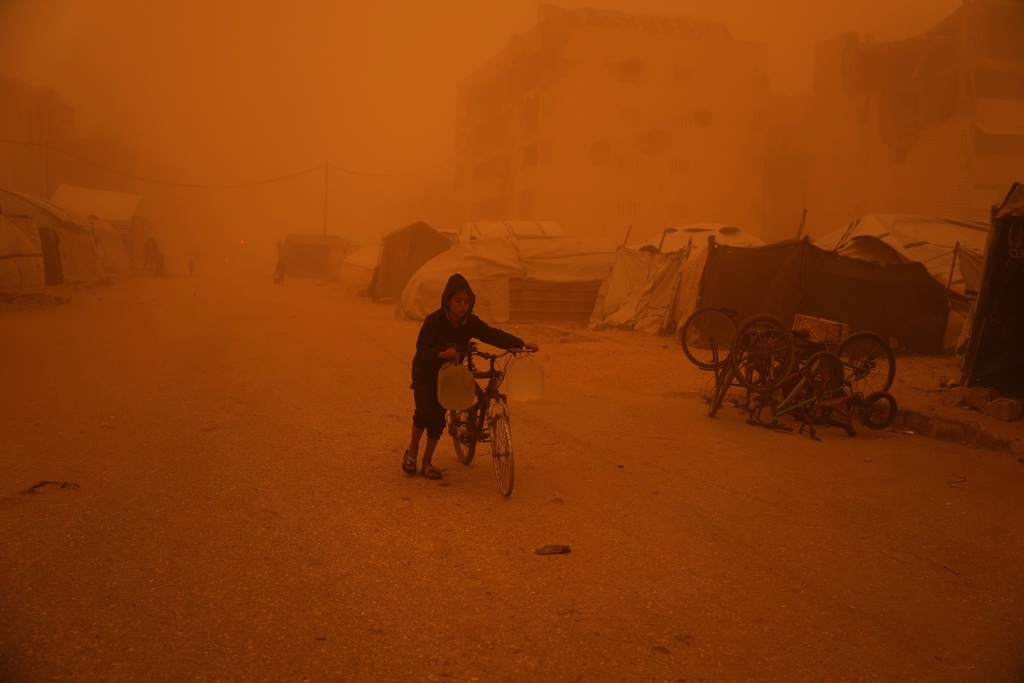 A boy pushes a bicycle carrying jerrycans of water through a sandstorm in Khan Younis, southern Gaza Strip, Saturday, March 14, 2026. (AP Photo/Abdel Kareem Hana)