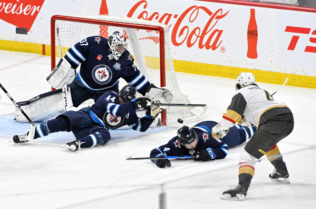 Winnipeg Jets' Josh Morrissey (44) and Neal Pionk (4) slide to block a shot on goaltender Connor Hellebuyck (37) by Vegas Golden Knights' Rasmus Andersson (4) during the third period of their NHL hockey game in Winnipeg, Tuesday, March 24, 2026. (Fred Greenslade/The Canadian Press via AP)