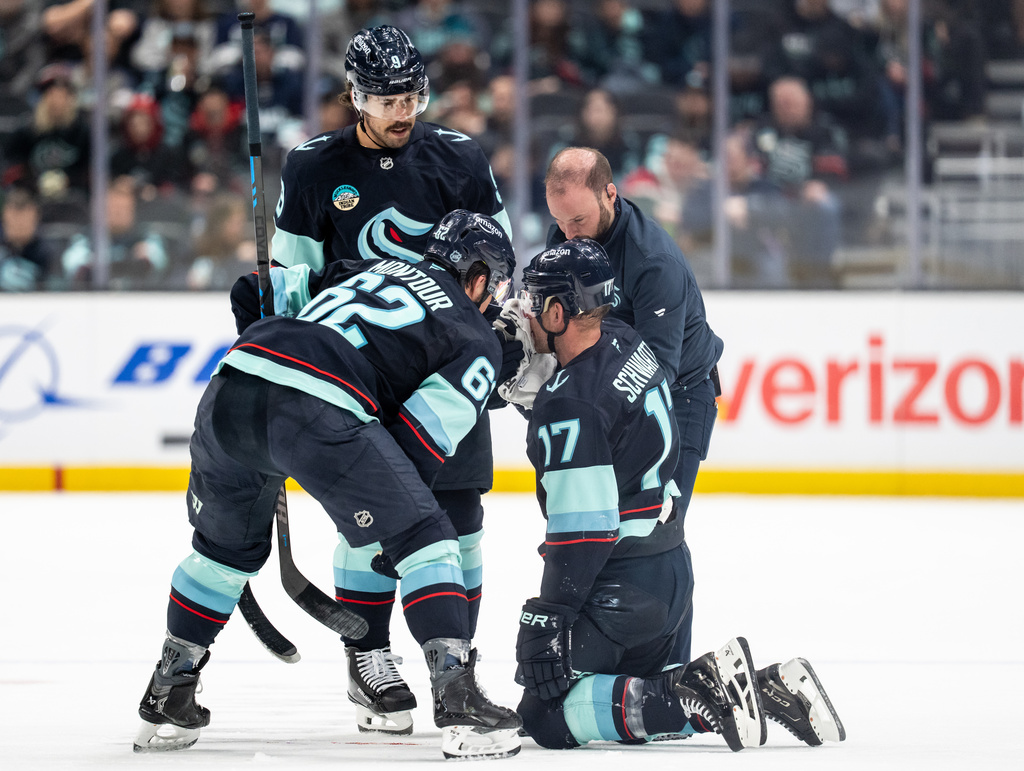 Seattle Kraken forward Jaden Schwartz (17) is tended to by team personnel and teammates defenseman Brandon Montour (62) and forward Chandler Stephenson (9) after a collision during the first periodof an NHL hockey game against the Ottawa Senators Saturday, March 7, 2026, in Seattle. (AP Photo/Stephen Brashear)