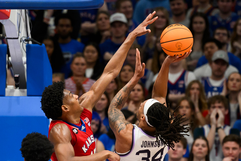 Kansas forward Bryson Tiller, left, blocks a shot by Kansas State guard Nate Johnson (34) during the first half of an NCAA college basketball game in Lawrence, Kan., Saturday, March 7, 2026. (AP Photo/Reed Hoffmann)