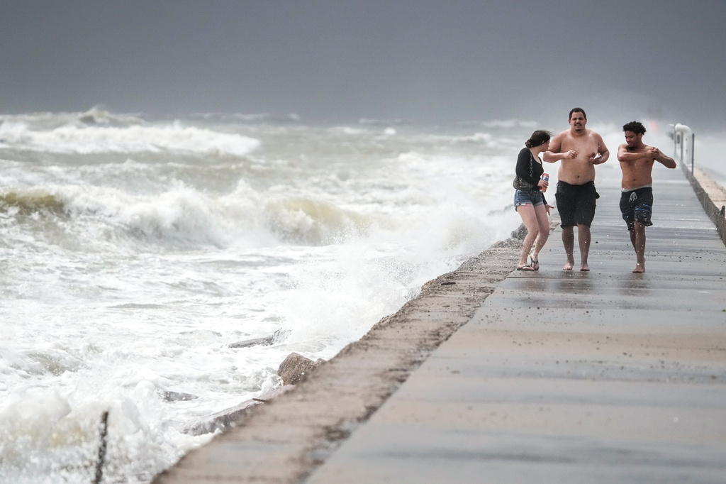 Lelania Martinez, left, Gregory Heath and Ethan Garza walk along the jetty as heavy surf stirred up by Tropical Storm Arthur batters the beach in Surfside, Texas, Wednesday, June 17, 2026. (Brett Coomer/Houston Chronicle via AP)
