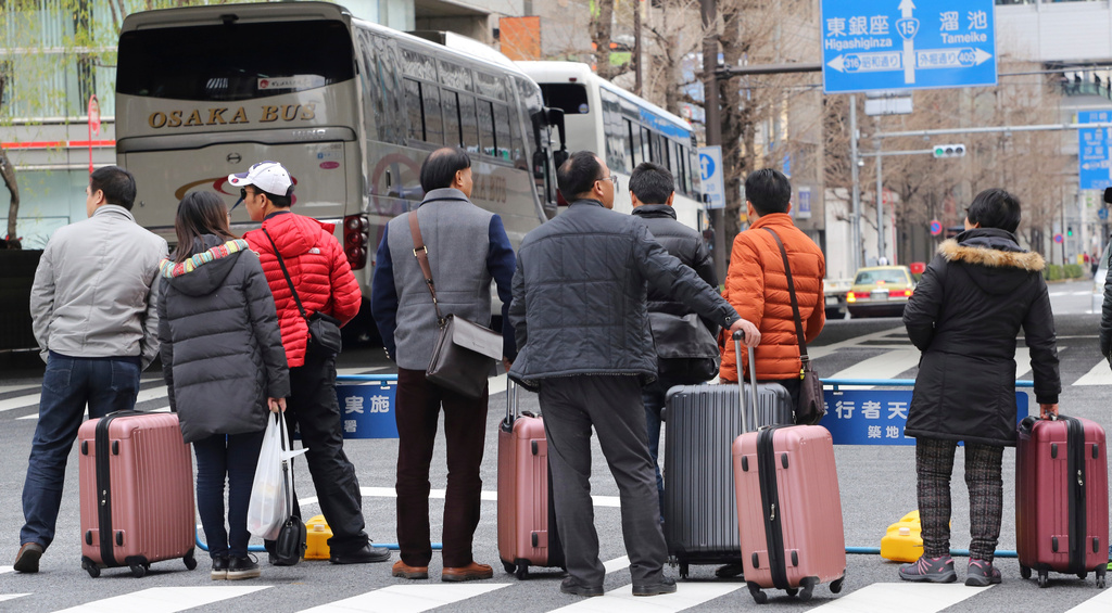 FILE - Chinese tourists wait for a bus at the Tokyo's Ginza shopping district in Tokyo, Saturday, March 12, 2016. (AP Photo/Koji Sasahara, File)