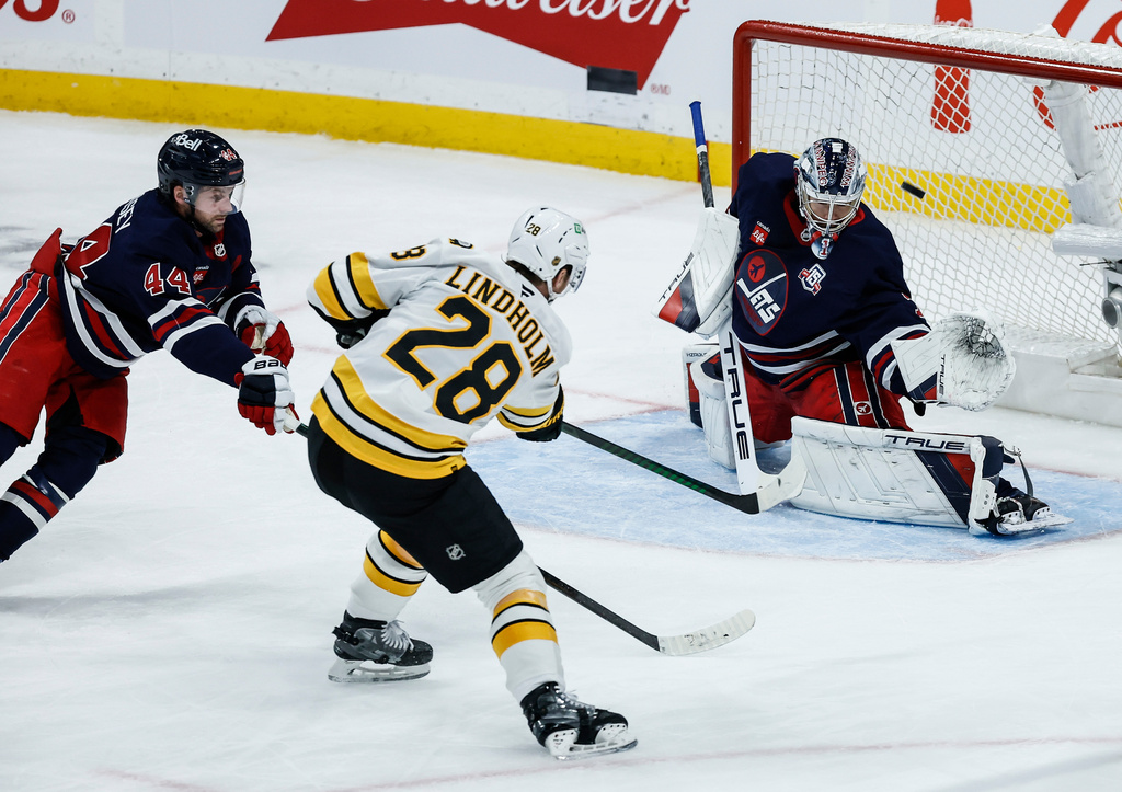 Winnipeg Jets' Josh Morrissey (44) defends against Boston Bruins' Elias Lindholm (28) as he scores on goaltender Eric Comrie (1) during the third period of an NHL hockey game, in Winnipeg, Manitoba, Thursday, Dec. 11, 2025. (John Woods/The Canadian Press via AP)