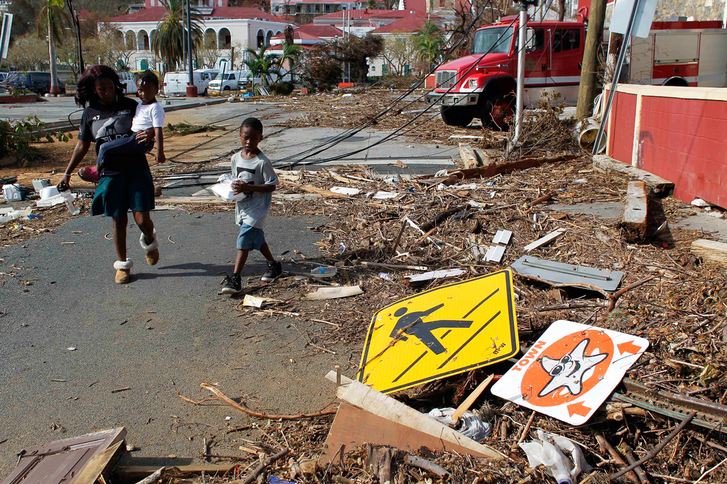 FILE - A woman and her children walk past debris left by Hurricane Irma in Charlotte Amalie, St. Thomas, U.S. Virgin Islands, on Sept. 10, 2017. (AP Photo/Ricardo Arduengo, File)
