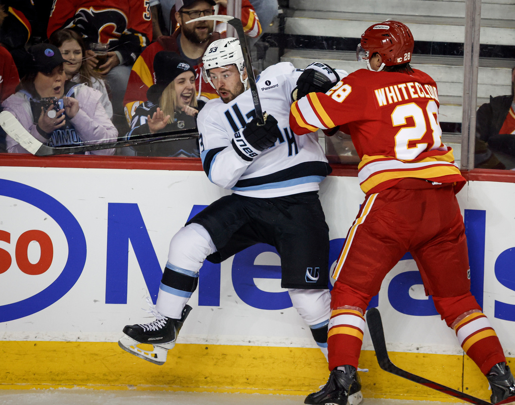 Utah Mammoth's Michael Carcone, left, is checked by Calgary Flames' Zach Whitecloud during first period NHL hockey action in Calgary, Alberta, Sunday, April 12, 2026. (Jeff McIntosh/The Canadian Press via AP)