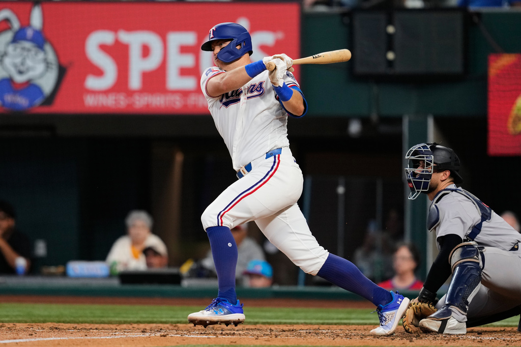 Texas Rangers' Josh Jung follows through on a two-run single as New York Yankees catcher J.C. Escarra, right, looks on in the fifth inning of a baseball game Wednesday, April 29, 2026, in Arlington, Texas. (AP Photo/Tony Gutierrez)