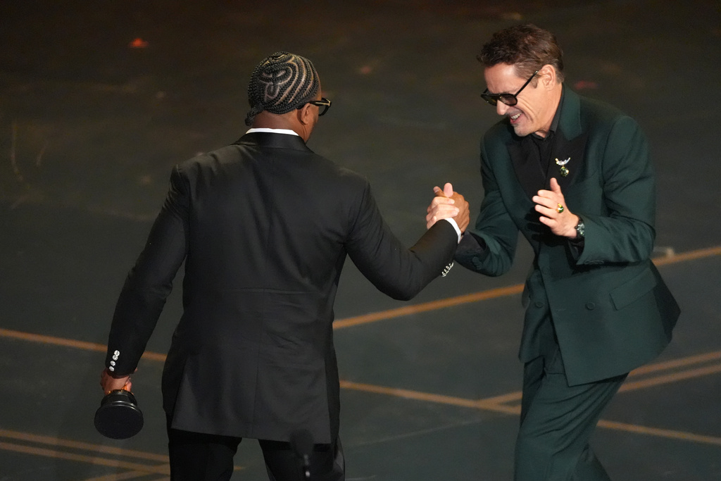 Robert Downey Jr., right, congratulates Ryan Coogler for winning the award for writing (original screenplay) for "Sinners" during the Oscars on Sunday, March 15, 2026, at the Dolby Theatre in Los Angeles. (AP Photo/Chris Pizzello)