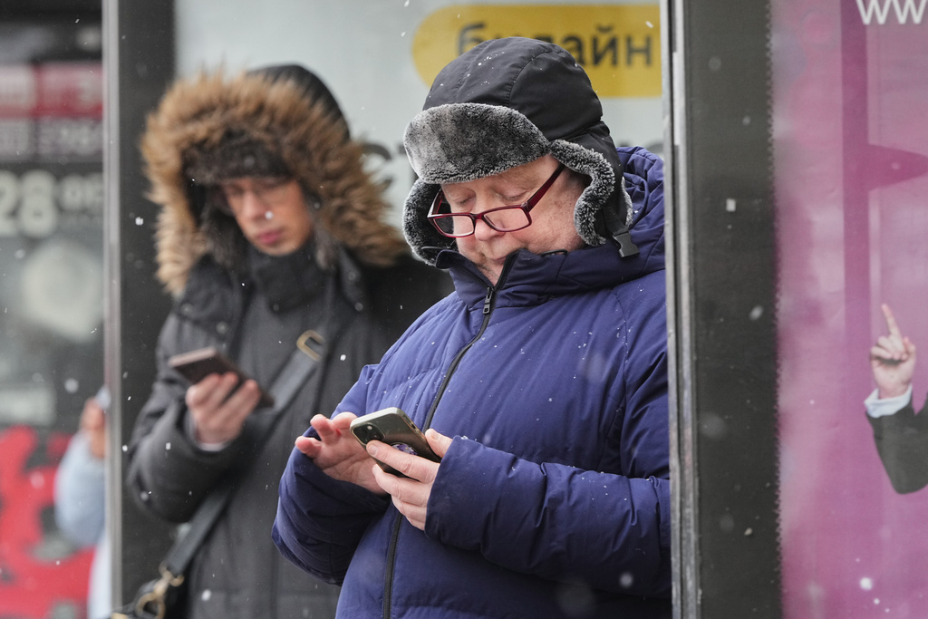 People look at their smartphones at a bus stop in St. Petersburg, Russia, Wednesday, Feb. 11, 2026. (AP Photo/Dmitri Lovetsky)