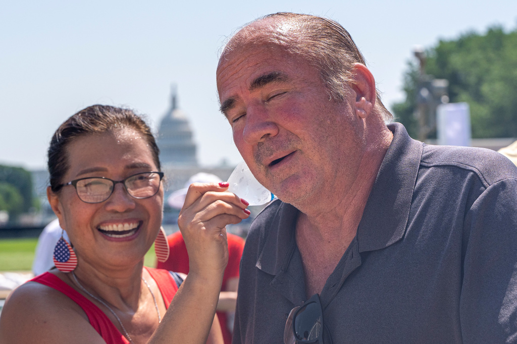 Stephanie McCallister holds a cold bottle of water to her husband Don McCallister's neck as they wait in line for the ferris wheel at the Great American State Fair on the National Mall, Wednesday, July 1, 2026, in Washington. (AP Photo/Jen Golbeck)