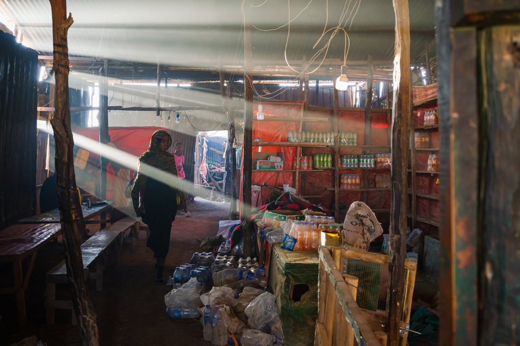 Burning myrrh, which is done to deter bugs and snakes, mingles with cooking smoke in a dark roadside restaurant as a young woman walks by bottles of water and soda Thursday, Jan. 8, 2026, in Afcadde, Ethiopia. (AP Photo/Julianne Gauron)