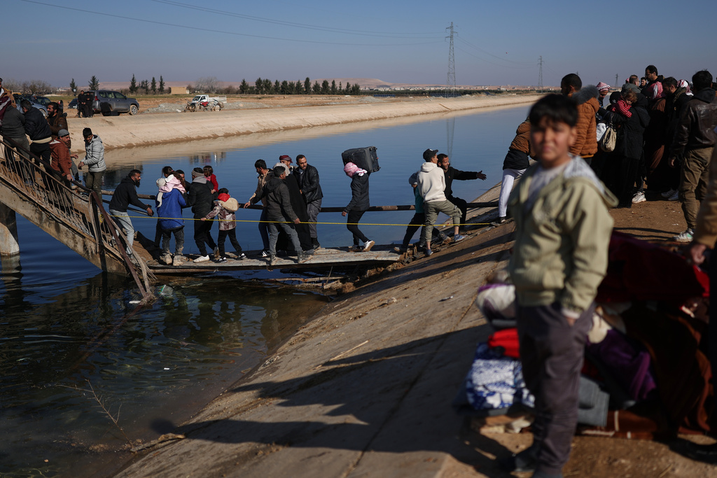 Displaced Syrians walk to cross at a river crossing near the village of Rasm al-Harmil al-Imam in the eastern Aleppo countryside, near the front line with the Kurdish-led Syrian Democratic Forces, in Deir Hafer, Syria, Friday, Jan. 16, 2026. (AP Photo/Ghaith Alsayed)