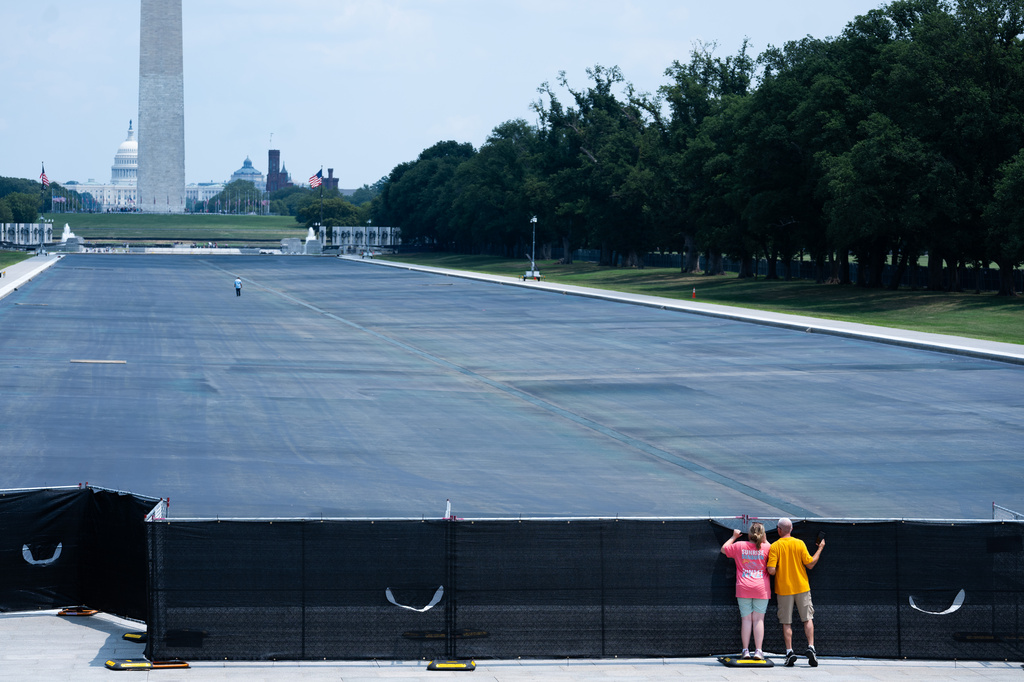 Individuals peek over the fence to see the drained Lincoln Memorial Reflecting Pool,, Monday, July 27, 2026, in Washington. (AP Photo/Allison Robbert)