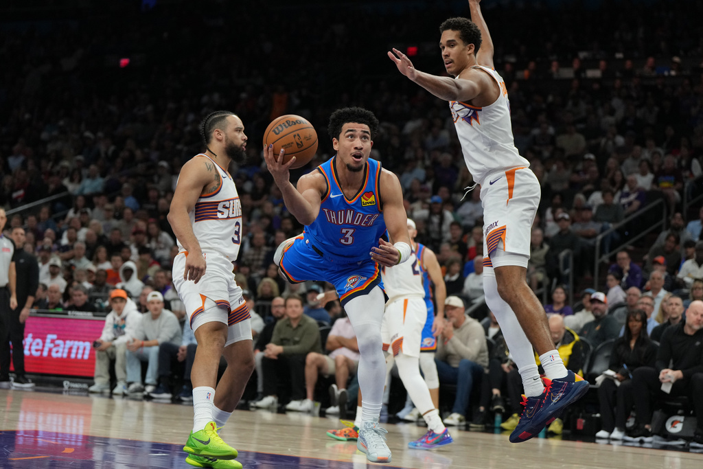 Oklahoma City Thunder guard Jared McCain scores between Phoenix Suns forward Dillon Brooks (3) and forward Oso Ighodaro during the first half of an NBA basketball game, Wednesday, Feb. 11, 2026, in Phoenix. (AP Photo/Rick Scuteri)