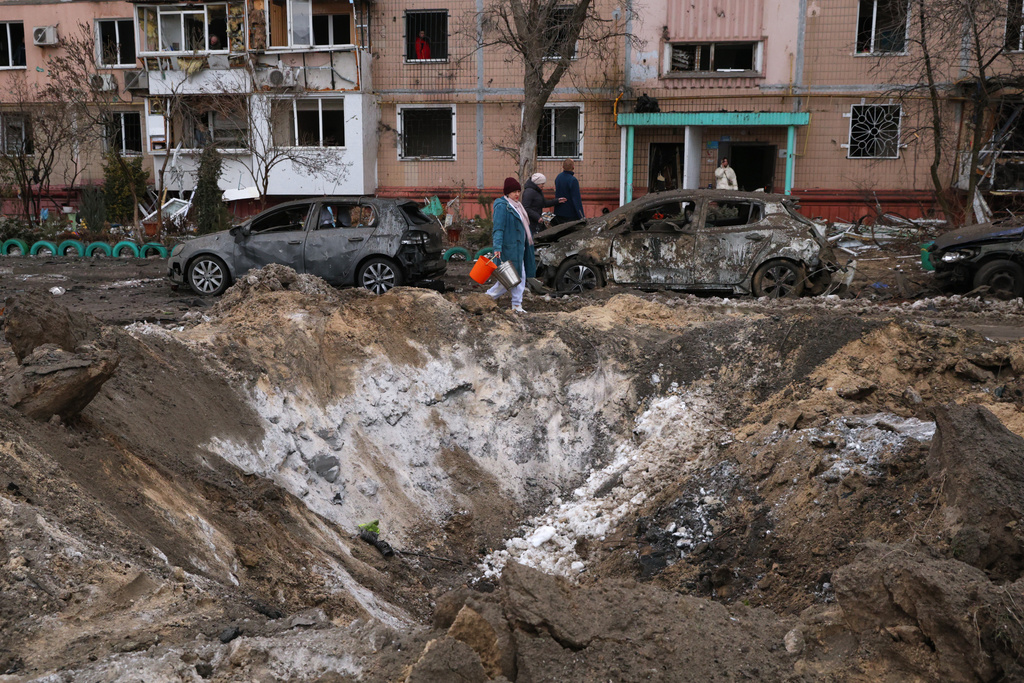 People pass a crater and damaged cars near an apartment building after a Russian attack in Zaporizhzhia, Ukraine, Wednesday, Jan. 28, 2026. (AP Photo/Kateryna Klochko)