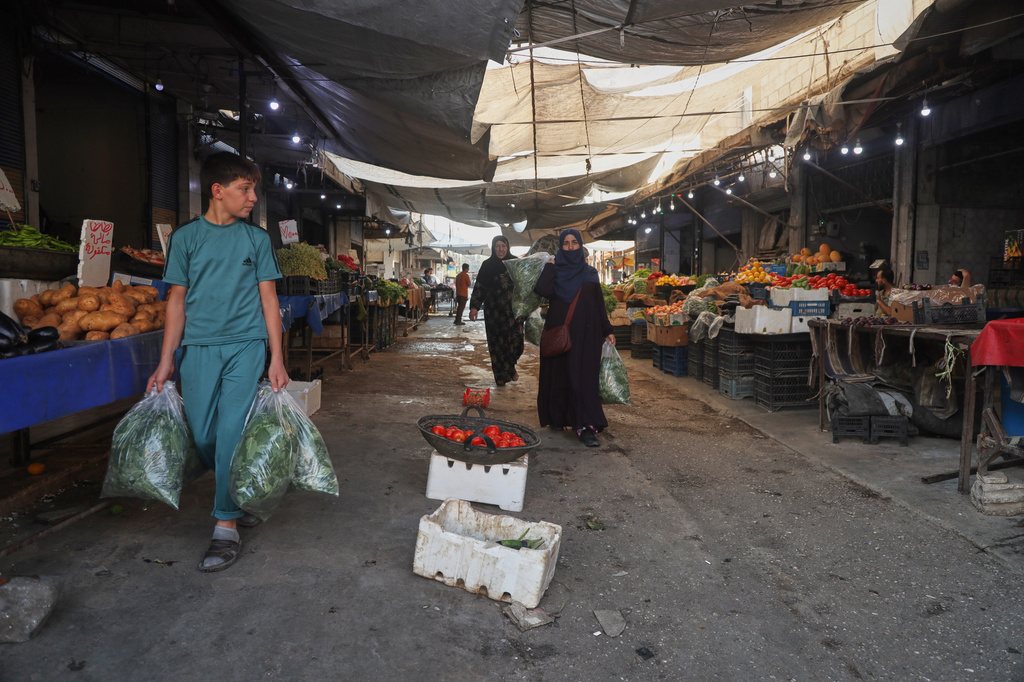 Residents carry bags of leafy greens past produce stalls at a market in Qamishli, northeastern Syria, Wednesday, Aug. 26, 2026. (AP Photo/Baderkhan Ahmad)