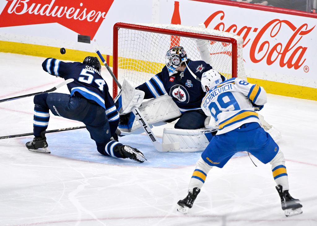 St. Louis Blues' Pavel Buchnevich (89) has a shot deflected wide of Winnipeg Jets' goaltender Eric Comrie (1) and Dylan Samberg (54) during the third period of their NHL hockey game in Winnipeg, Tuesday, Jan. 20, 2026. (Fred Greenslade/The Canadian Press via AP)