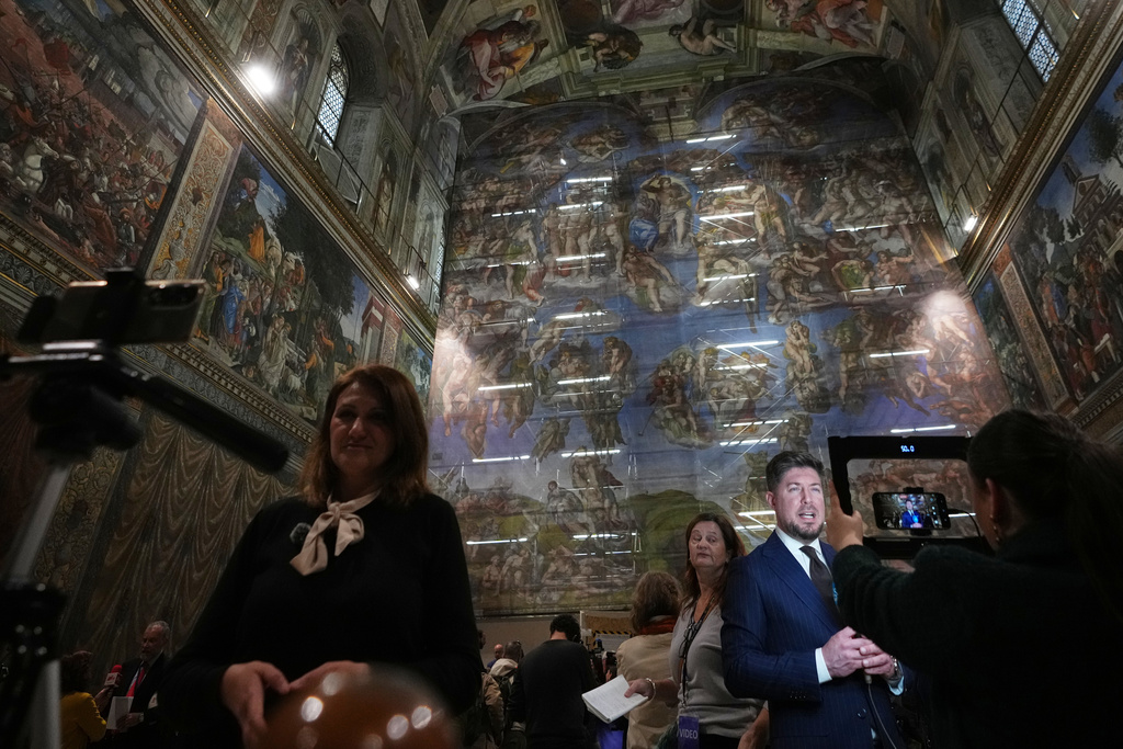 Journalists report in front of a screen with a replica of “The Last Judgment,” superimposed on it that covers the scaffolding used for its extraordinary maintenance, during the presentation for press in the Sistine Chapel at the Vatican, Saturday, Feb. 28, 2026. (AP Photo/Alessandra Tarantino)